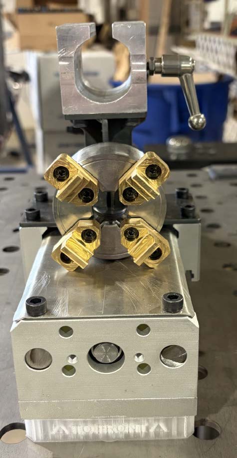 Close-up photograph of the sample holder showing custom tailstock and multiple mini lathe chucks with brass jaws
